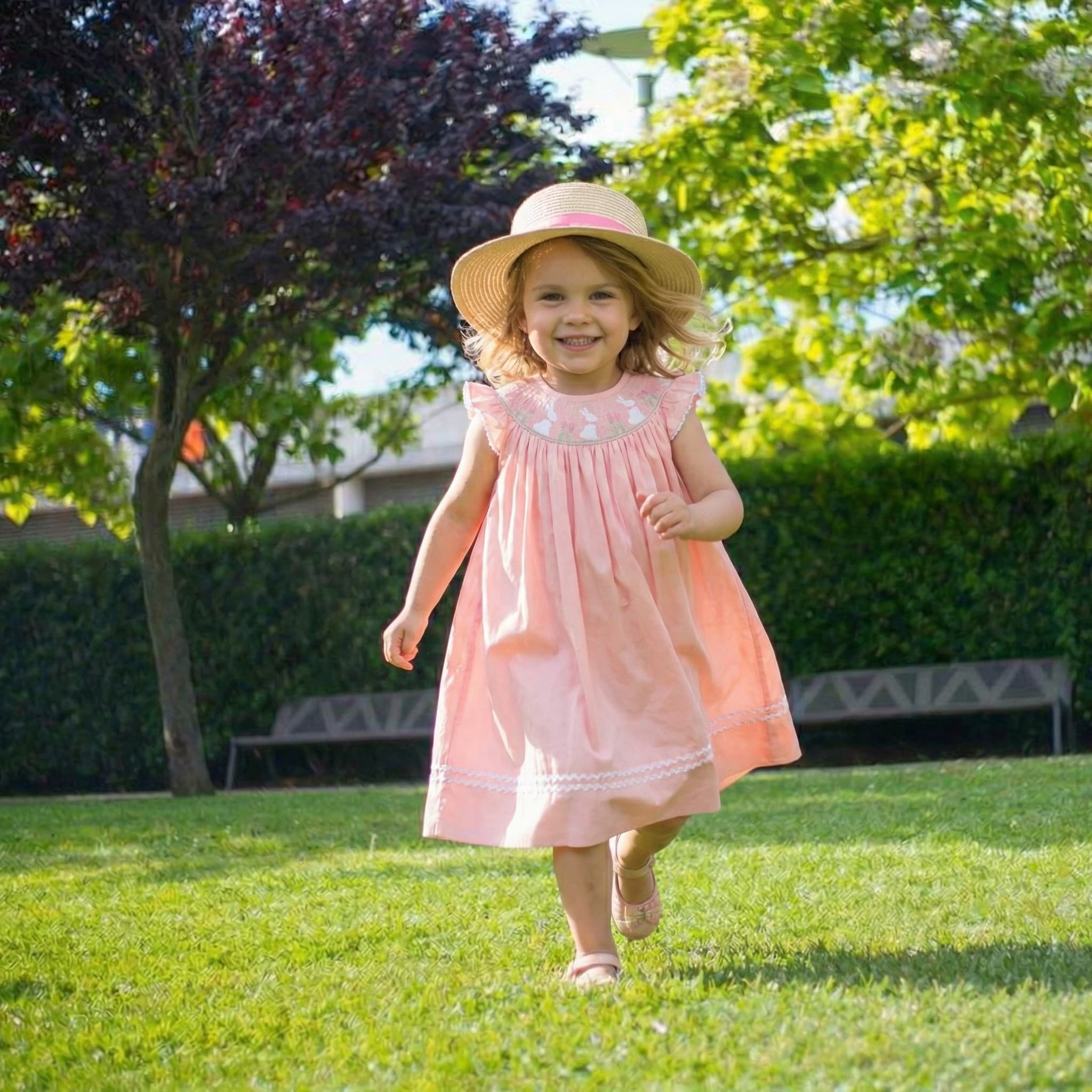 Little girl in pink embroidered dress running in garden